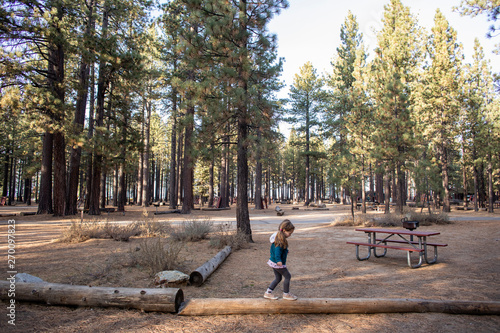 A young girl balancing on a log at a campsite in the woods.