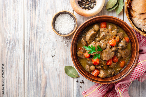 Turkey meat stew with mushrooms and vegetables in ceramic bowl on wooden table. Top view. Copy space.