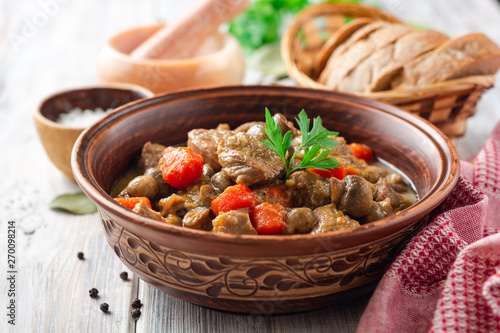 Turkey meat stew with mushrooms and vegetables in ceramic bowl on wooden table. Selective focus.