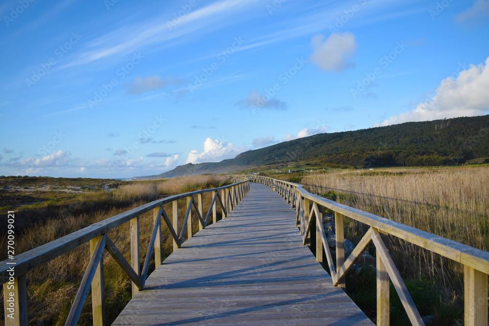 Paisaje pasarela de madera en medio del campo y de unos humedales entre el mar y las montañas. Paisaje pasarela de madera en medio del campo y de unos humedales entre el mar y las montañas.