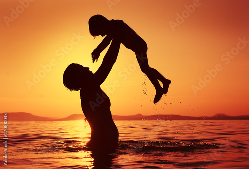 Mother lift her lovely child in water at sunset