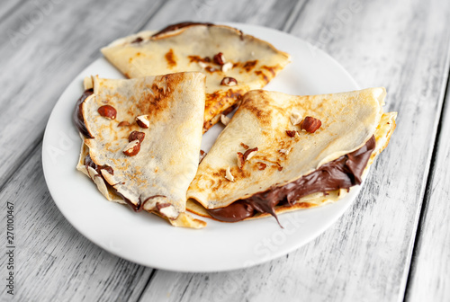 Pancakes with chocolate spread and hazelnuts,  on a white plate on a wood background
