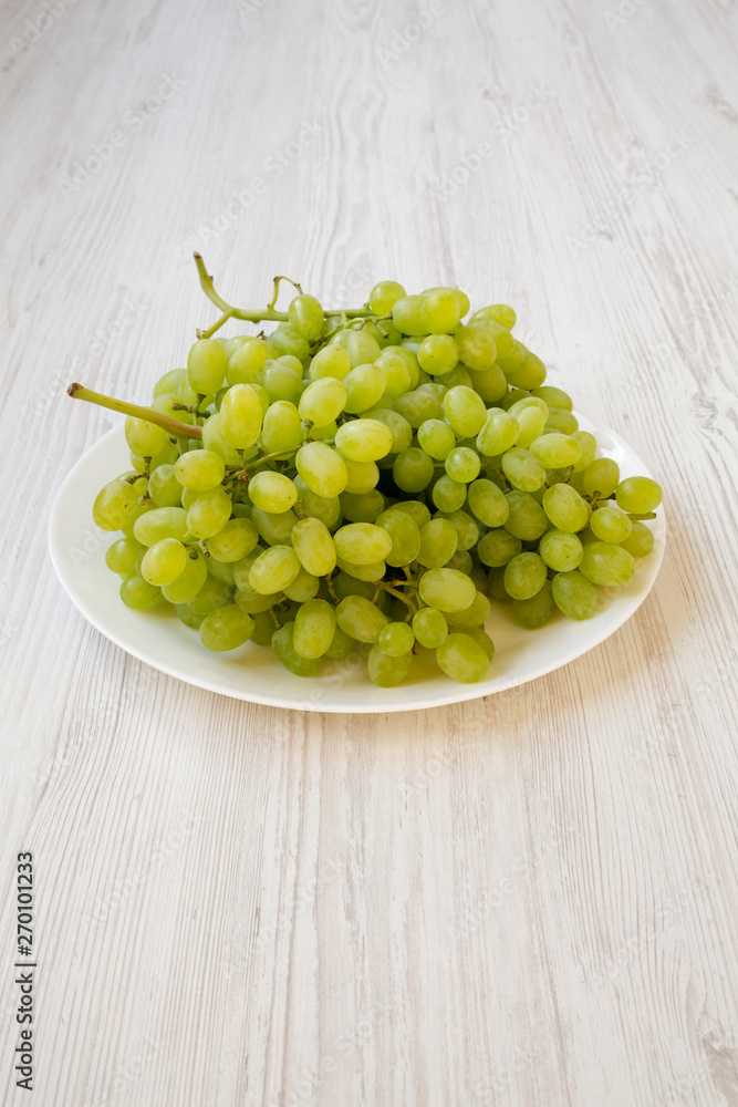 Green grape on a white plate over white wooden background, side view. Green grape on a white plate over white wooden background, side view.