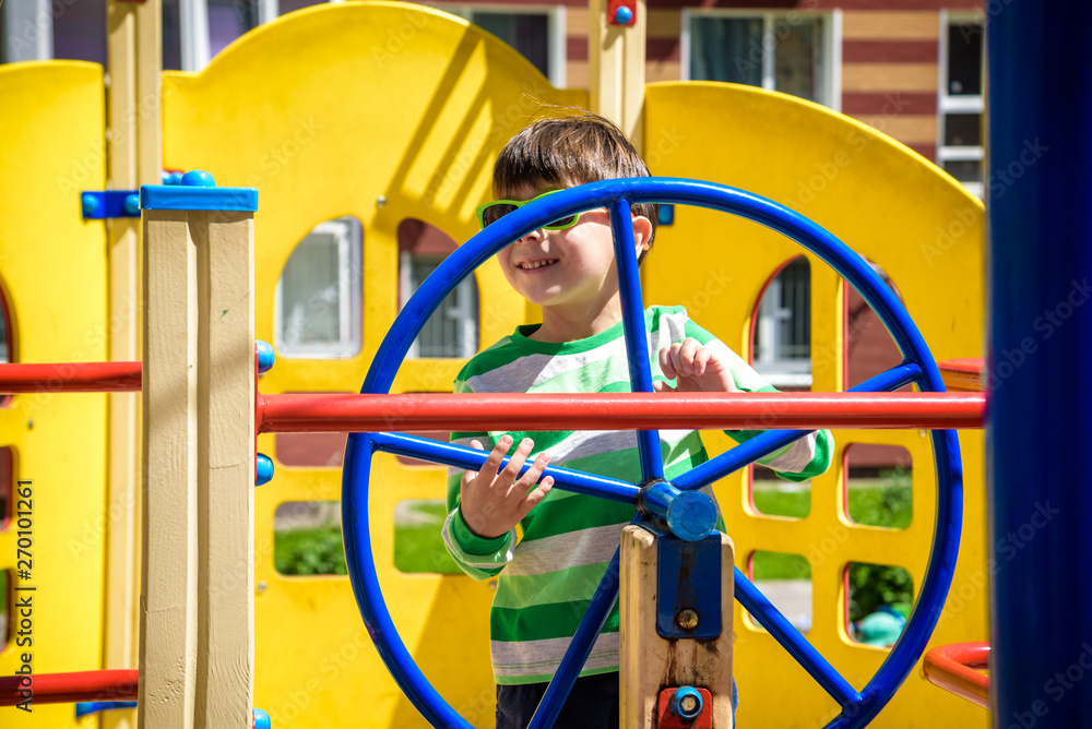 Boy as a captain or sailors play on the ship outdoors on sunny day. Kid has a lot of fun. Ship has colorful flags on wind Boy as a captain or sailors play on the ship outdoors on sunny day. Kid has a lot of fun. Ship has colorful flags on wind