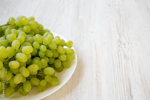 Green grape on a white plate over white wooden background, side view. Copy space.