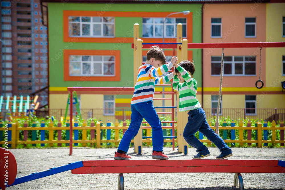 Two little school and preschool kids boys playing on playground outdoors together. children having competition standing on log with outdoor activities in summer sunny day