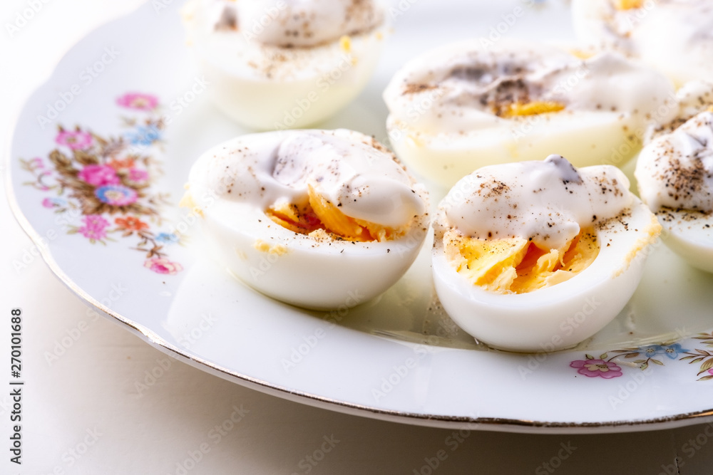 Sliced boiled eggs with mayonnaise and pepper in white plate isolated close up Sliced boiled eggs with mayonnaise and pepper in white plate isolated close up