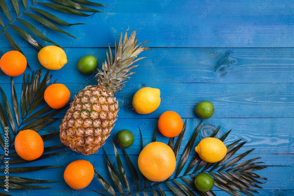 Pineapple, orange, lemon, grapefruit, lime and palm leaves on blue wooden background Pineapple, orange, lemon, grapefruit, lime and palm leaves on blue wooden background