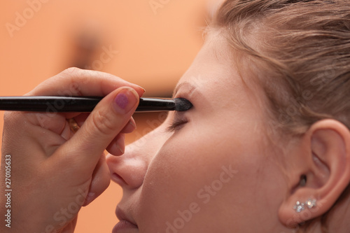 Close up face of young bride, artist doing make up. Bride has scar on eybrow after piercing. photo