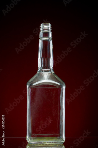 Transparent empty alcohol bottle on red background