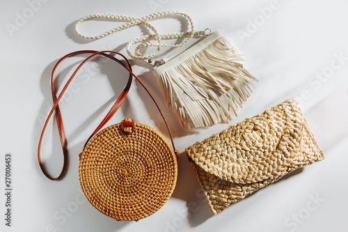 Variety summer handbags on white background. Round bamboo bag, handbag with fringe and straw bag. Flat lay, top view. Fashion concept. photo