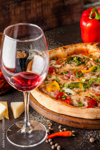 Concept Italian cuisine. A real pizza with vegetables and ham, bacon and parmesan cheese. The ingredients on the table. Red wine in a glass on the table. Closeup, background image
