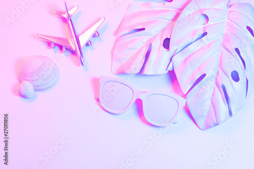 Traveler duotone accessories on glowing neon background with retro camera  sunglasses  seashells  airbus and tropical palm leaf. Flat lay minimal retrowave concept. Summer background.