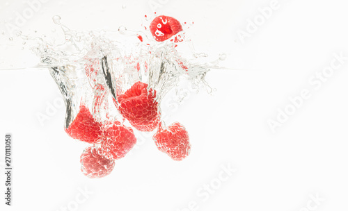 Fresh raspberries falling in water on white background