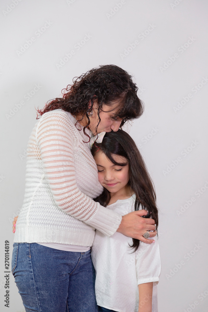 Mom hugging her little daughter and giving her a kiss on the forehead tenderly- Latina mom and daughter Mom hugging her little daughter and giving her a kiss on the forehead tenderly- Latina mom and daughter
