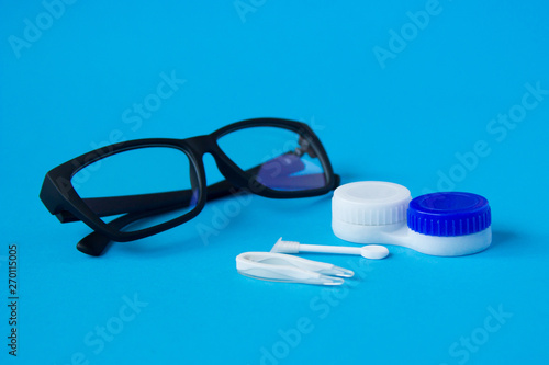 Glasses and container with contact lenses on a blue background. The concept of taking care of vision.