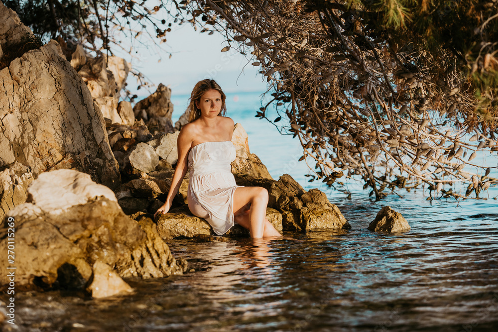 Beautiful young pregnant woman with white wet dress relax on the rocks