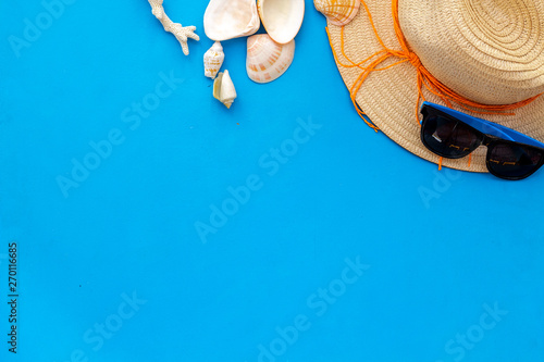 Planning vacation to the seaside with straw hat, sun glasses, shells on blue background top view space for text