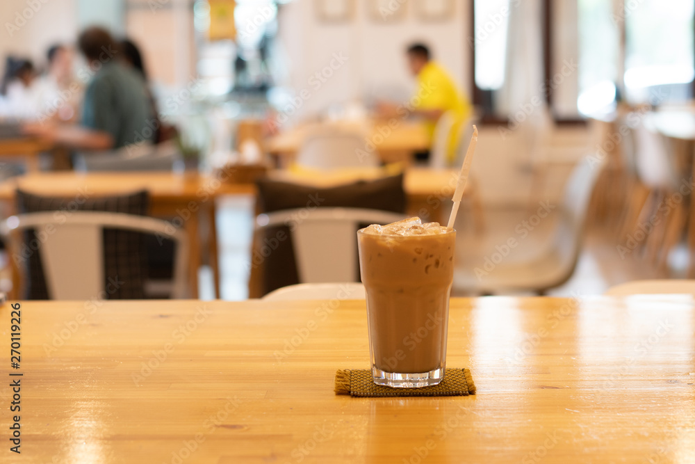 Ice coffee in glass, placed on a wooden table in a coffee shop. The customers sit in the cafe blurred background