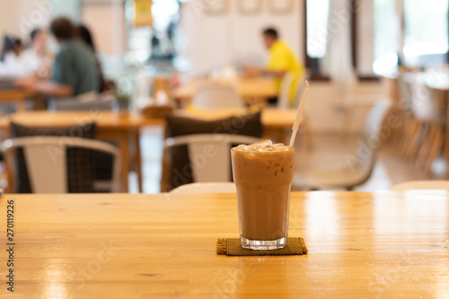 Ice coffee in glass  placed on a wooden table in a coffee shop. The customers sit in the cafe blurred background