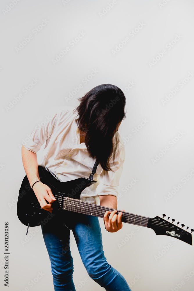 Young long haired guitarist excited playing his black electric guitar, isolated on white background. Young long haired guitarist excited playing his black electric guitar, isolated on white background.