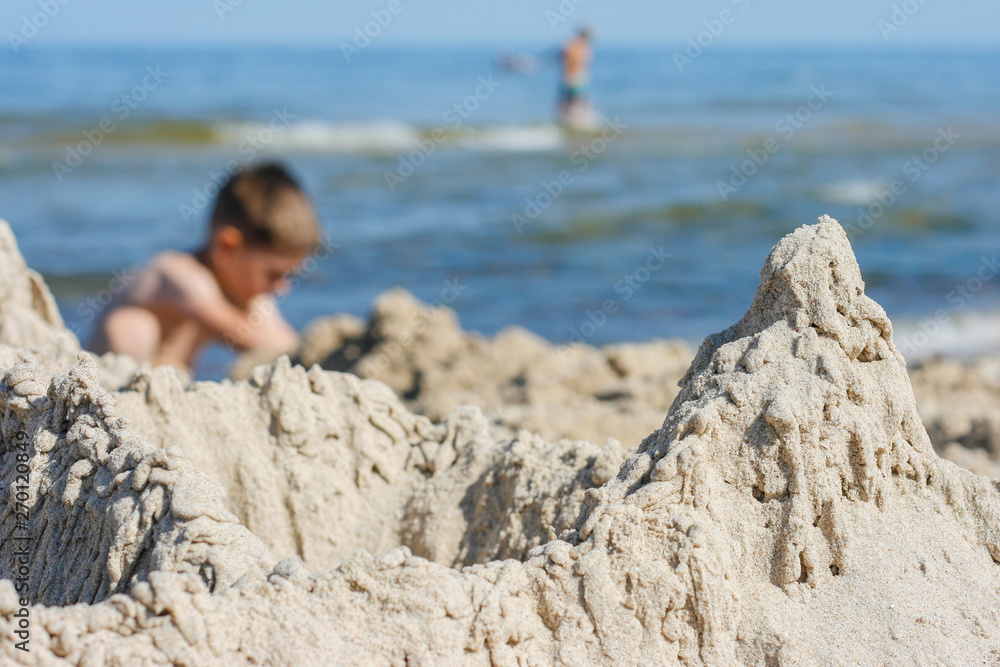 Kind spielt am Strand. Sandburg im Vordergrund