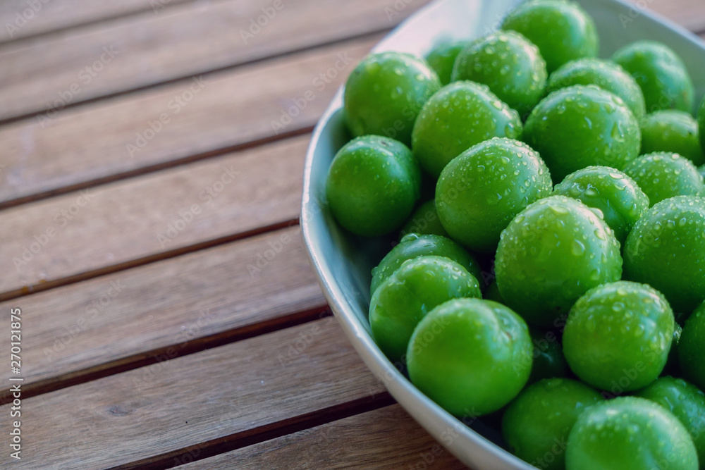 Green plums in white dish on wooden background close up view with copyspace Green plums in white dish on wooden background close up view with copyspace