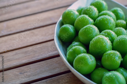 Green plums in white dish on wooden background close up view with copyspace