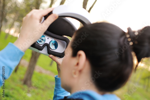 young woman in a virtual reality helmet on the background of greenery and Park. VR glasses