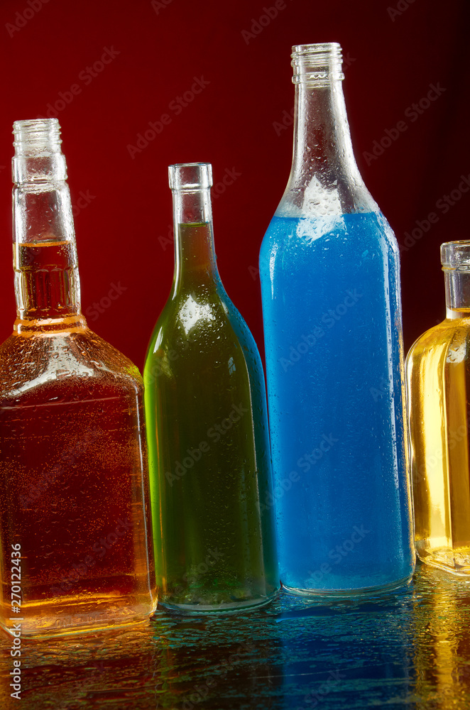 Alcohol bottles in water drops on red background Alcohol bottles in water drops on red background
