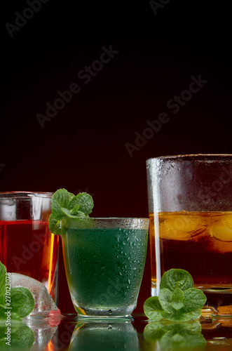 Three different alcoholic drinks in clear glasses with ice and mint on red background