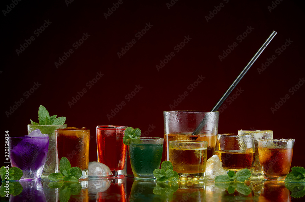 Different alcoholic drinks in clear glasses with ice and mint on red background Different alcoholic drinks in clear glasses with ice and mint on red background