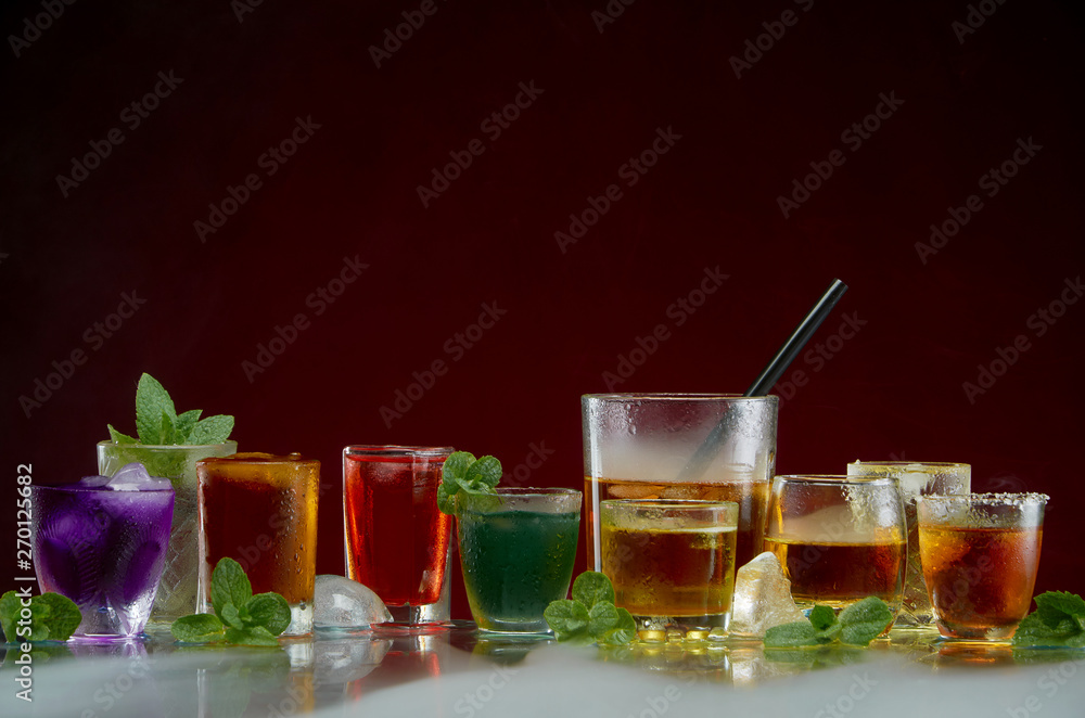 Glasses with various alcoholic drinks with ice and mint on red background Glasses with various alcoholic drinks with ice and mint on red background