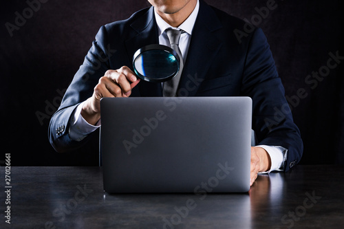 虫眼鏡でノートパソコンを見るビジネスマン