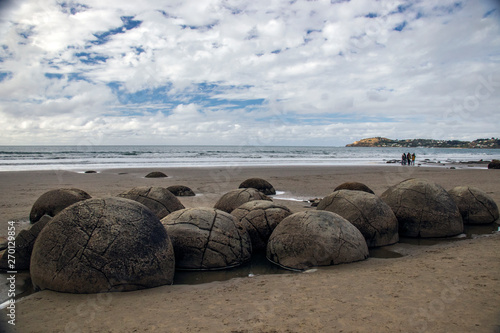 Large and spherical boulders lying along a stretch of Koekohe Beach Otago coast with cloudy sky and sea background in South Island of New Zealand between Moeraki and Hampden 