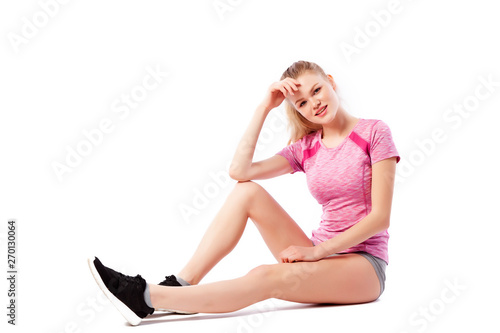 Sport exercises on a white background, fitness concept. Young woman in comfortable sportswear (shorts and top) smiling, sitting on the floor and posing on white isolated background
