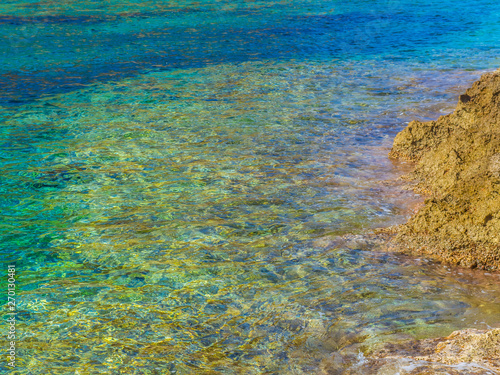 Beautiful azure blue clear water and a yellow rocky shore