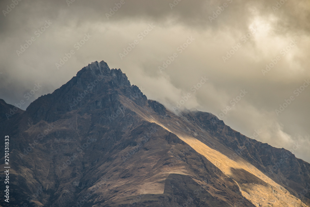 sunlit mountain top view under clouds around Lake Wakatipu at Queenstown on the South Island of New Zealand