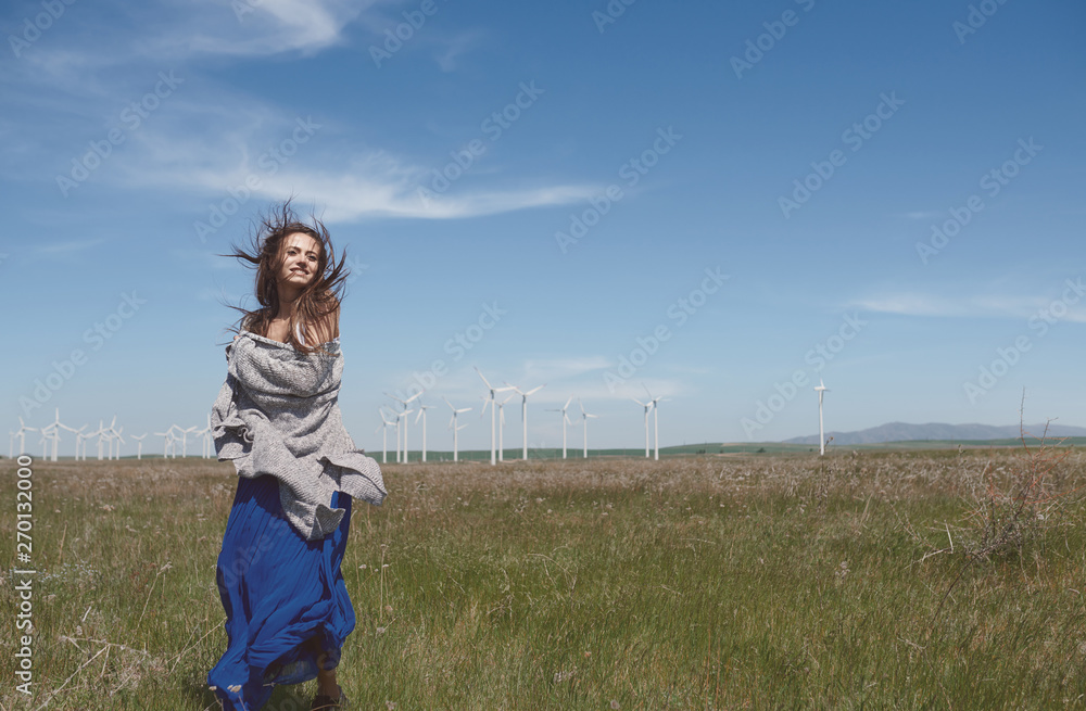 Woman with long tousled hair next to the wind turbine with the wind blowing Woman with long tousled hair next to the wind turbine with the wind blowing