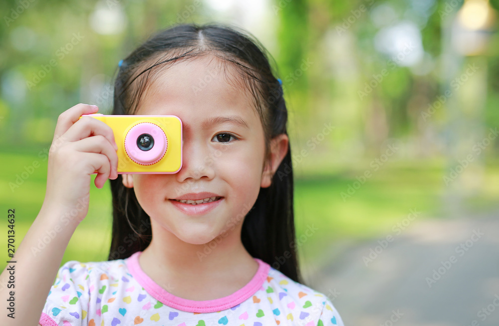 Portrait of smiling little girl takes photo with digital camera toy in the garden outdoor. Portrait of smiling little girl takes photo with digital camera toy in the garden outdoor.