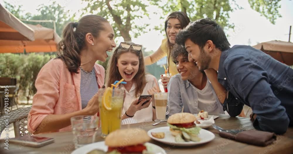 Five multiethnic friends sitting at table in cafe, talking on phone with someone, then cheering and highfiving. People enjoying theit time together 4k Five multiethnic friends sitting at table in cafe, talking on phone with someone, then cheering and highfiving. People enjoying theit time together 4k