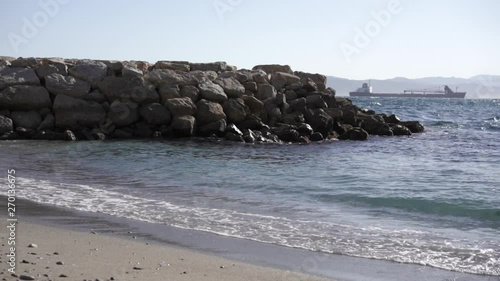 Waves wash in to a sandy bay in Gibraltar, with a cargo ship in the background