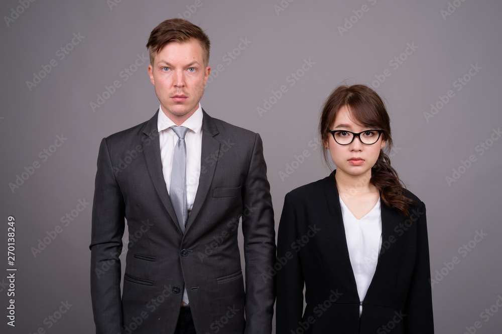 Young businessman and young Asian businesswoman against gray bac