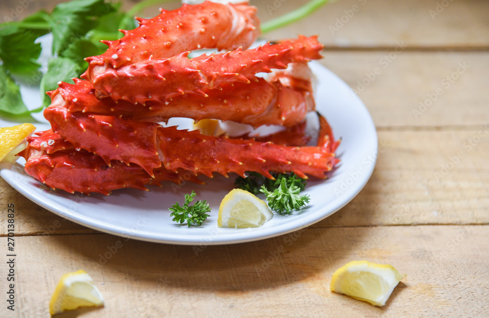 Alaskan King Crab Legs cooked seafood with lemon spices on white plate in the wooden table - red crab hokkaido Alaskan King Crab Legs cooked seafood with lemon spices on white plate in the wooden table - red crab hokkaido