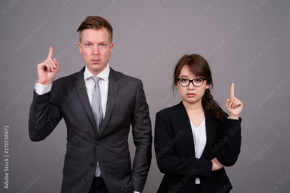 Young businessman and young Asian businesswoman against gray bac Young businessman and young Asian businesswoman against gray bac