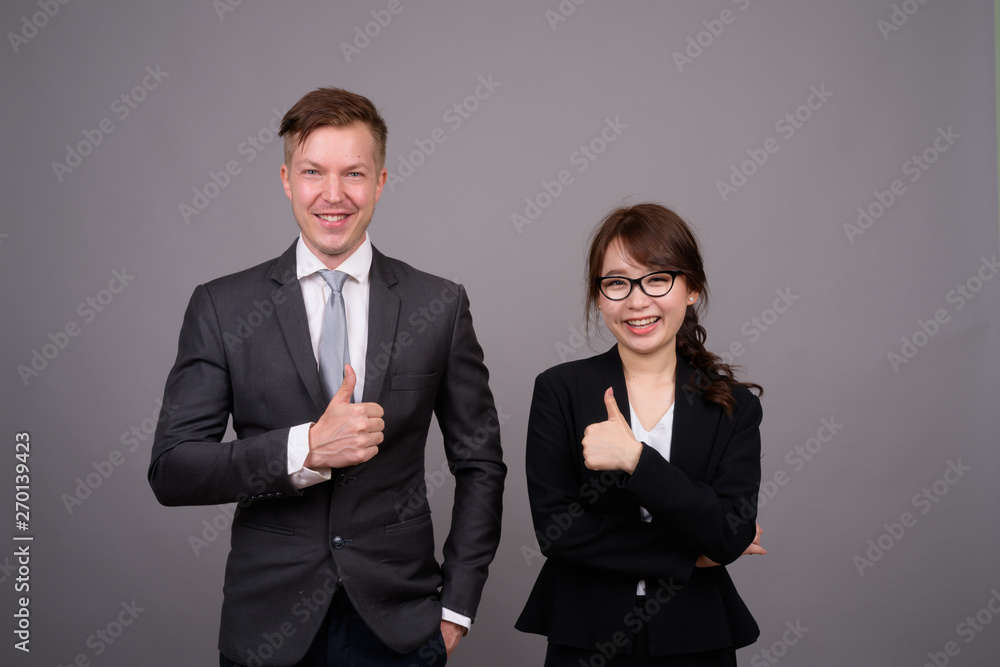 Young businessman and young Asian businesswoman against gray bac Young businessman and young Asian businesswoman against gray bac