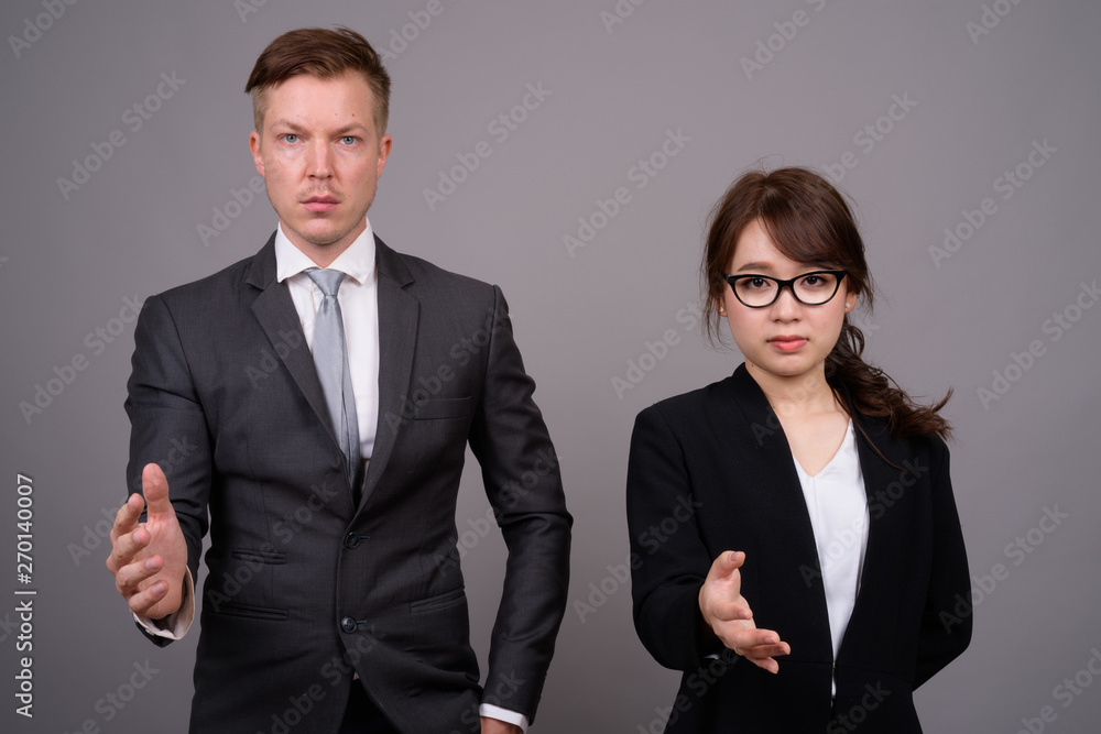 Young businessman and young Asian businesswoman against gray bac Young businessman and young Asian businesswoman against gray bac