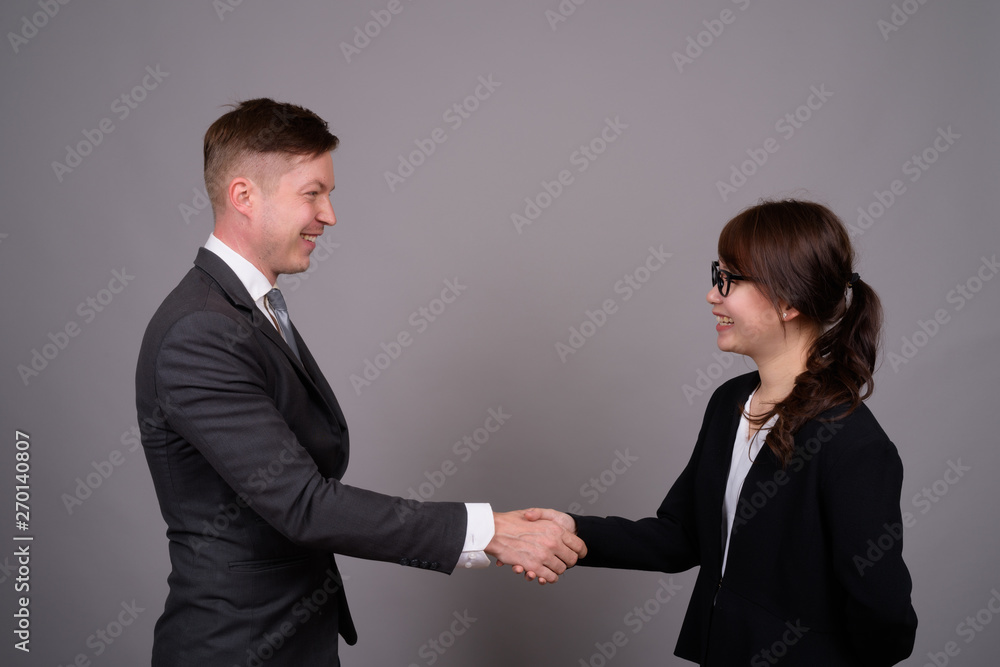 Young businessman and young Asian businesswoman against gray bac Young businessman and young Asian businesswoman against gray bac