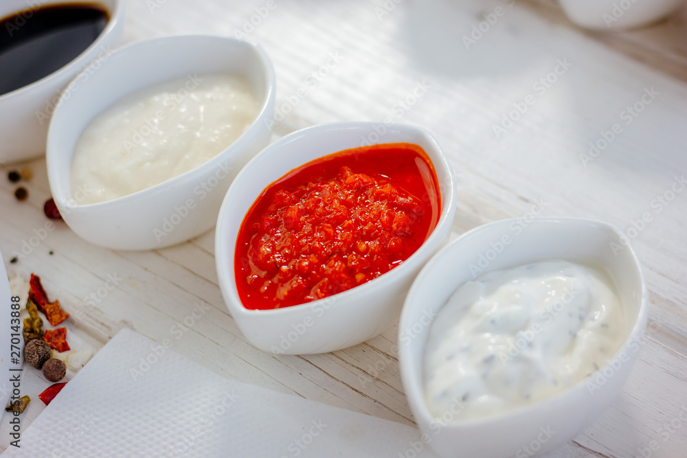 Different dips and sauces - red, white and black over white table. Different dips and sauces - red, white and black over white table.