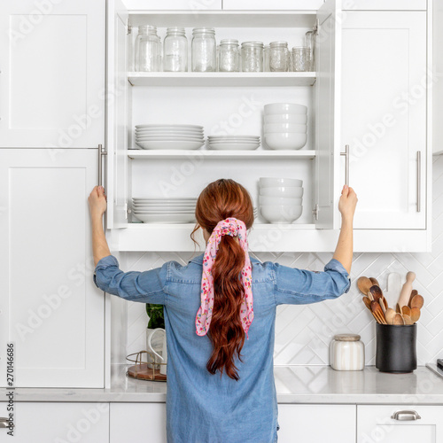 Foto A woman looking in a farmhouse kitchen cabinet full of white dishes